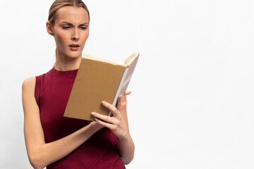 Obraz premium Confused woman in red sleeveless top reads a book with puzzled expression isolated on white background. Concept of misunderstanding, concentration, and learning challenges.