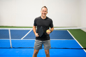 Positive men looking at camera while playing pickleball at court indoor