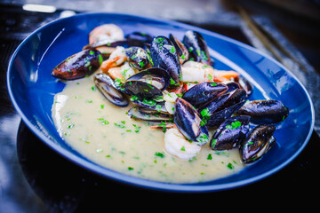 Apetyczne małże i krewetki w jasnym sosie podane na niebieskim talerzu. © Artur