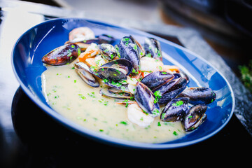 Apetyczne małże i krewetki w jasnym sosie podane na niebieskim talerzu. © Artur