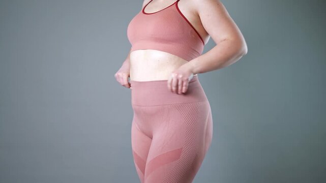 Fat woman in corrective tights, flabby belly after pregnancy, overweight female body on gray studio background