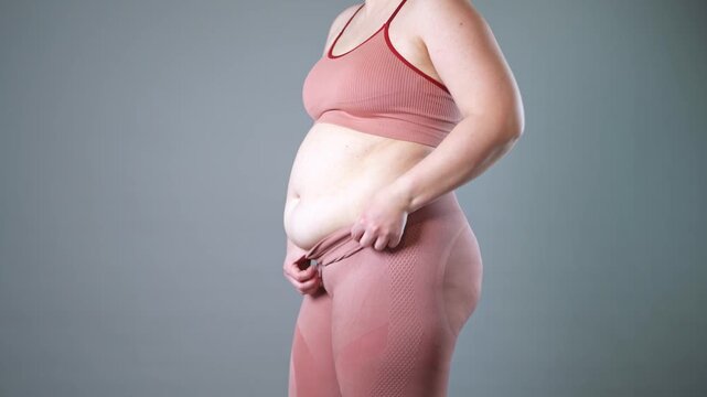 Fat woman in corrective tights, flabby belly after pregnancy, overweight female body on gray studio background