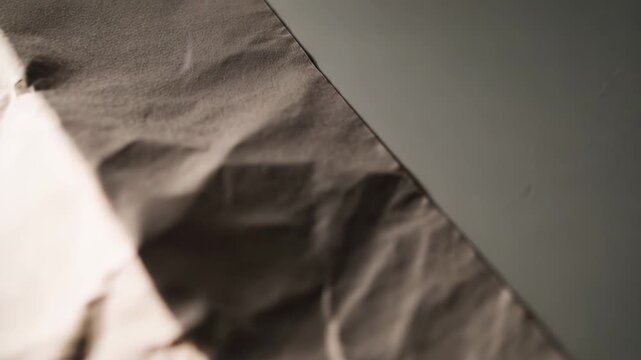 Crumpled paper texture creating an abstract pattern with creases and wrinkles, enhancing the warm vintage feel as sunlight casts a strong shadow diagonal across the surface