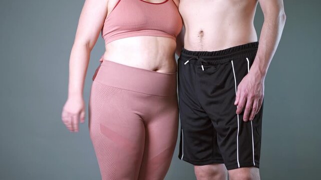 Couple doing stomach vacuum exercise, man and woman inhale and exhale their stomachs during a breathing exercise, breathwork and fitness, gray background