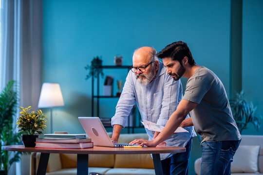Two Indian generations reviewing income reports and submitting taxes online at home using laptop