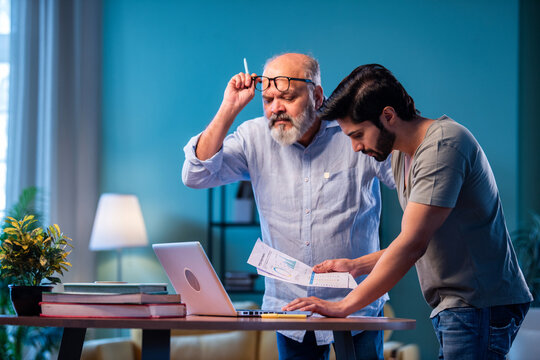 Two Indian generations reviewing income reports and submitting taxes online at home using laptop
