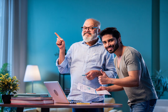 Two Indian generations reviewing income reports and submitting taxes online at home using laptop