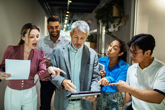 Multigenerational coworkers reviewing tablet in office hallway