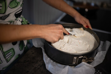 Obraz premium Woman spreading cream cheese batter in springform cake pan