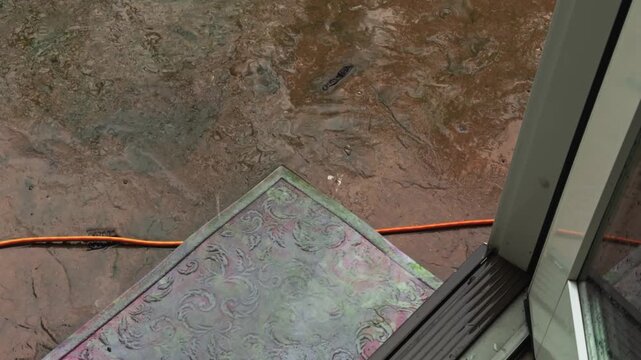 Orange Extension Cord Running Under an Old Doormat During Heavy Rain