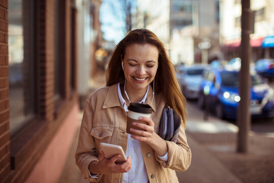 Smiling young woman with coffee and smartphone walking in city