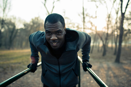 Athletic man doing tricep dips on parallel bars in a park at sunrise