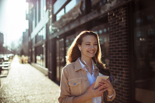 Smiling young woman with earbuds walking downtown