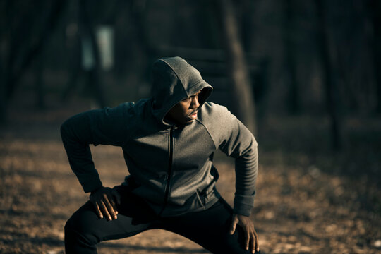 Man stretching in hoodie during outdoor workout in forest park