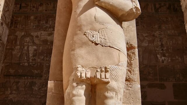 Medinet Habu temple first courtyard with Osiride pillars and Ramses III statues in mummy form in Luxor Egypt, hieroglyphic covered walls and ancient pharaonic colonnade.