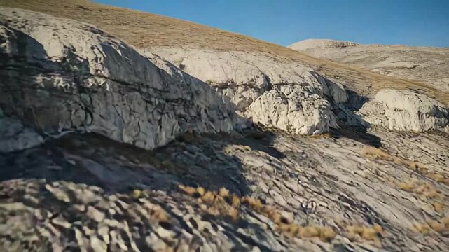 Arid mountain slope with exposed rock formations and patches of golden dry grass, illustrating challenging terrain and the vastness of wilderness landscapes