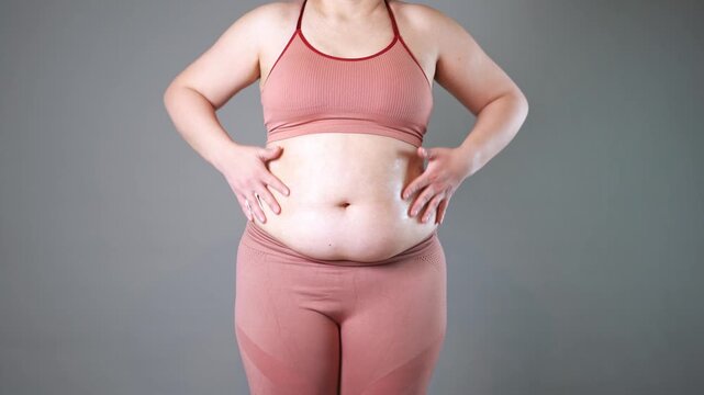 Abdominal massage, tummy tuck and flabby skin on a fat belly, woman doing self-massage with cream on gray studio background
