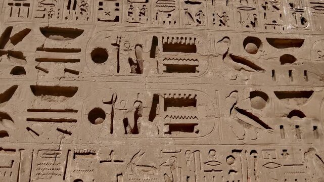 Closeup of ancient Egyptian hieroglyphic inscriptions with cartouches and bird symbols carved in sandstone wall at Medinet Habu temple in Luxor Egypt, detailed royal text.
