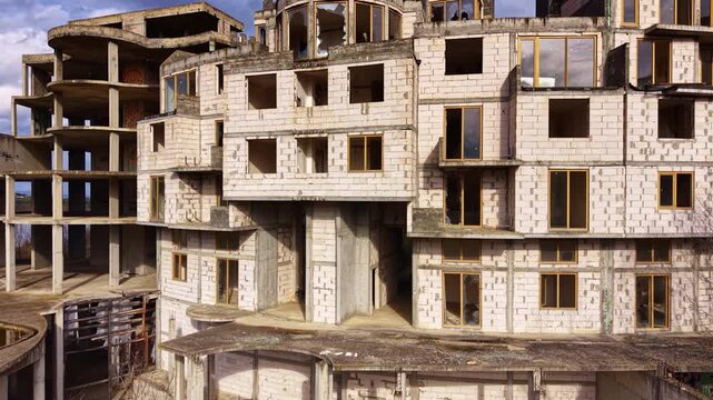 Crumbled concrete and unfinished walls create an eerie scene at a deserted building site, where nature slowly reclaims space amid overcast skies and shadows of the past.