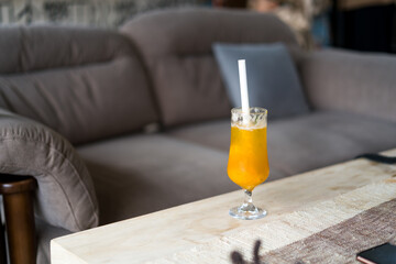 Orange beverage with straw on wooden coffee table in living room setting