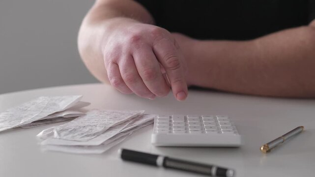 Man Carefully Arranging Business Documents With Calculator And Writing Instrument. Person Diligently Sorting And Organizing Financial Papers With Calculator And Pen At Desk