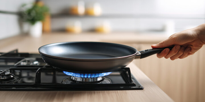 Hand holding empty frying pan over blue flame on gas stove, preparing to cook food in kitchen