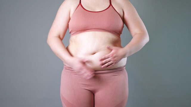 Abdominal massage, tummy tuck and flabby skin on a fat belly, woman doing self-massage with cream on gray studio background