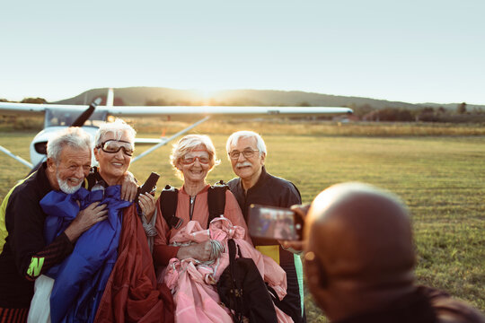 Senior friends posing after skydiving at an airfield at sunset