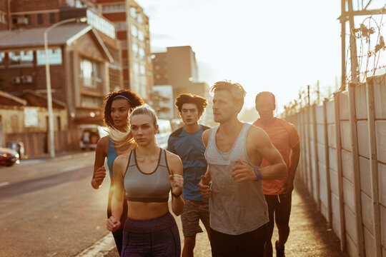 Group of runners training on city street at sunrise