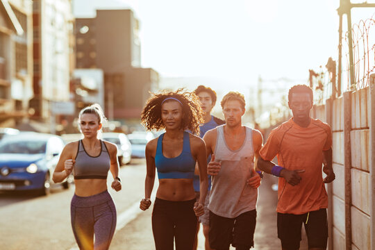 Diverse group of friends running on city street at sunrise