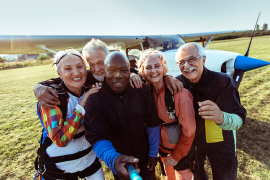 Happy senior skydivers taking selfie by airplane