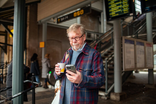 Senior man checking smartphone with coffee at train station