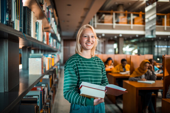 Smiling student holding books in university library
