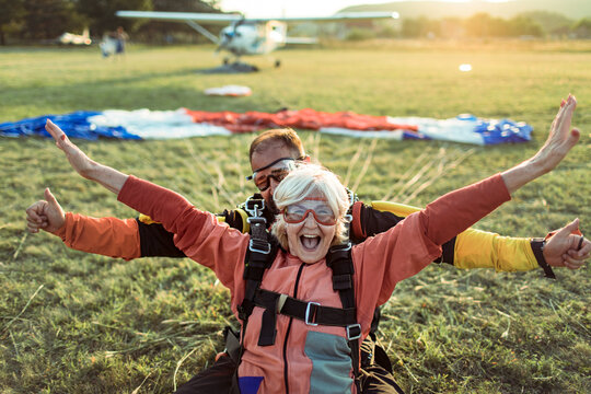 Joyful senior woman celebrating tandem skydive landing with instructor at airfield