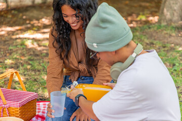 Young man pouring fresh orange juice into a glass held by a smiling young woman while enjoying a...