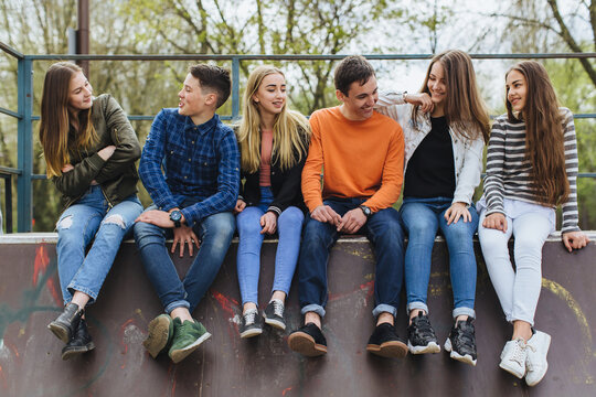 Group of diverse teenagers sitting together in a skate park, smiling and chatting, enjoying friendship and youth outdoors