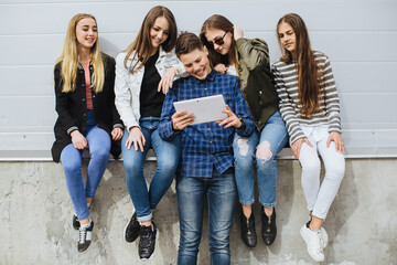 Fototapeta premium Diverse group of teenagers sitting on a ledge, smiling and sharing a digital tablet while browsing apps and chatting outdoors