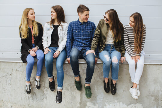 Group of diverse teenagers sitting together, laughing and talking outdoors, celebrating youth, friendship, and connection