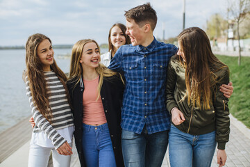 Diverse group of young teenagers walking outdoors by a lake, expressing joy, laughter, and strong...