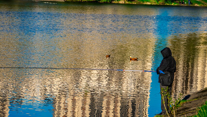 Angler Fishing by Rippling Water with Building Reflection and Ducks