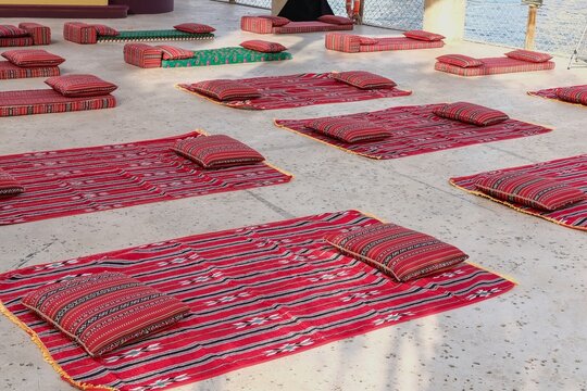 Traditional red Arabic carpets and cushions arranged on the floor in outdoor majlis style setting. Cultural Middle Eastern seating concept for gatherings, hospitality and heritage events.