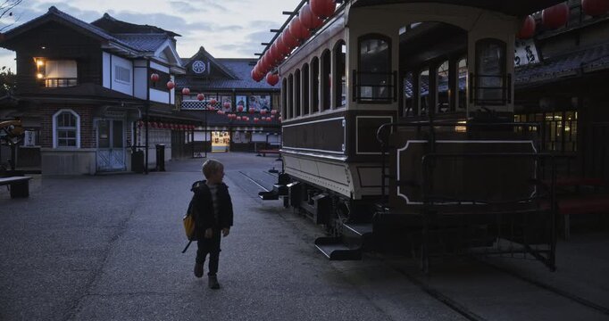 Happy boy walking through ancient Japanese village alone near tram at dusk