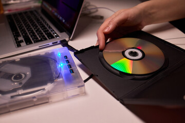 Careful handling of disc with external drive in background. Indoor environment showing detailed action of inserting disc into protective case with external device
