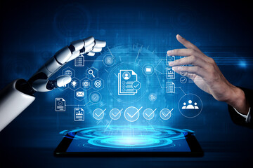 A human hand and a robotic hand reach towards a glowing digital interface that displays various...