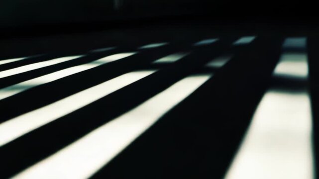 Dramatic parallel shadows and bright light stripes creating an abstract geometric pattern across a concrete or tiled surface, evoking a sense of mystery