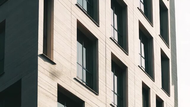 Building facade showcasing contemporary architectural design with stone cladding and rectangular windows reflecting sunlight, emphasizing urban aesthetics and geometric patterns under a clear sky