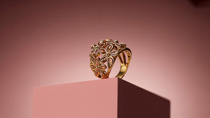Ornate gold ring with gemstones in vintage filigree design on pink pedestal in soft studio lighting for jewelry advertising