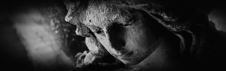 Fototapeta premium Close view of a sorrowful angel, eroded by time, reflecting grief, compassion, and acceptance of life’s fragile impermanence. Black and white image.
