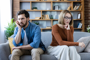 Upset man and woman experiencing relationship problems, sitting separate on a sofa with sad...