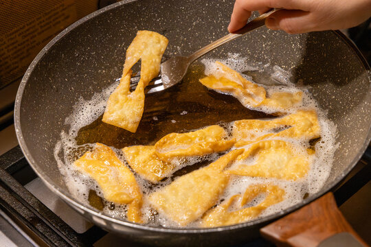 Frying traditional angel wings pastry known as faworki or chrust in hot oil inside a pan, crispy golden dough bubbles, homemade carnival sweet dessert.